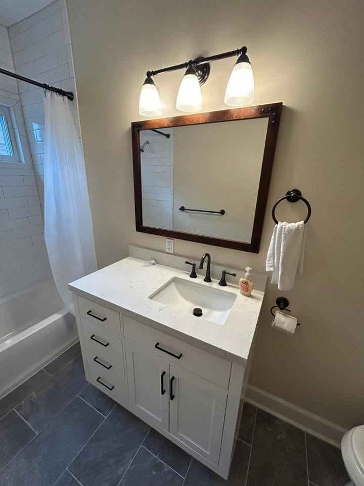 Completed bathroom with tiled shower, vanity, mirror, and updated fixtures