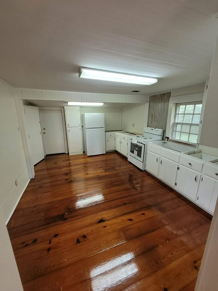 Finished kitchen with white cabinets, appliances, wood floors, and beadboard walls